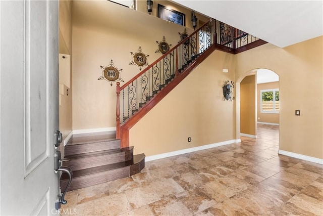 entryway featuring arched walkways, stairway, a high ceiling, and baseboards