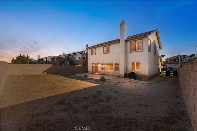 back of house at dusk with stucco siding, a patio, a fenced backyard, central AC unit, and a chimney