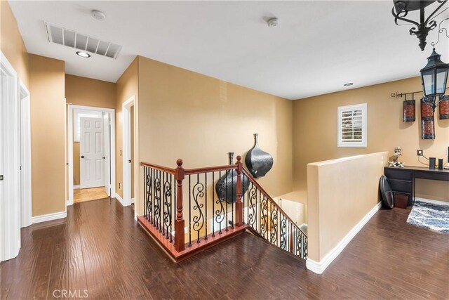 hall featuring baseboards, visible vents, dark wood finished floors, and an upstairs landing