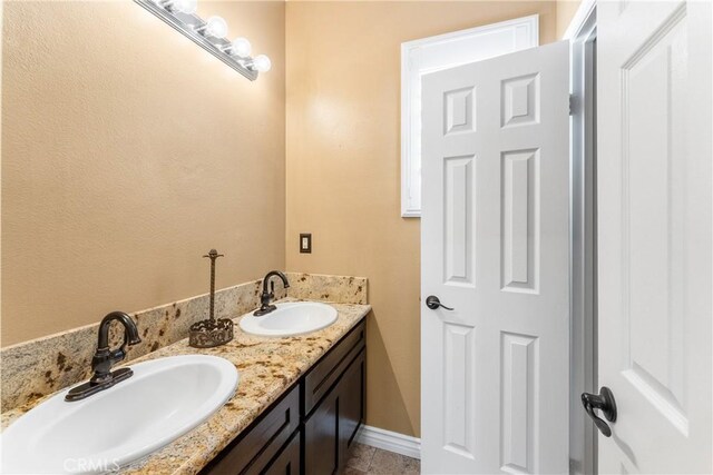 full bath with double vanity, baseboards, and a sink