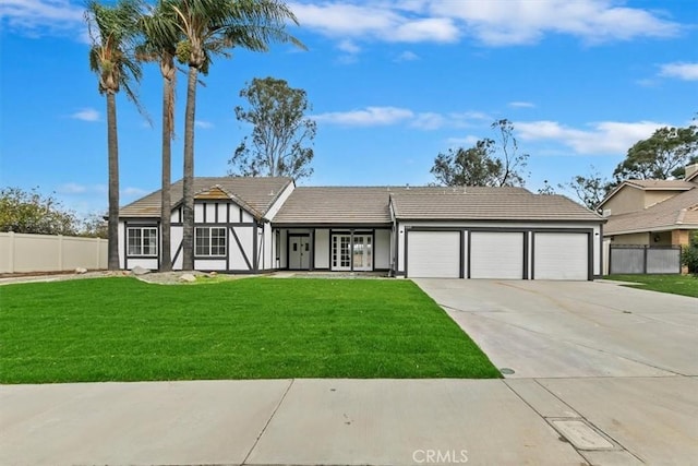 english style home with stucco siding, an attached garage, fence, driveway, and a front lawn