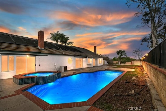 pool at dusk featuring a pool with connected hot tub, a patio area, fence, and central air condition unit