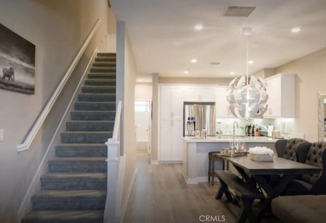 dining space with visible vents, an inviting chandelier, recessed lighting, wood finished floors, and stairs
