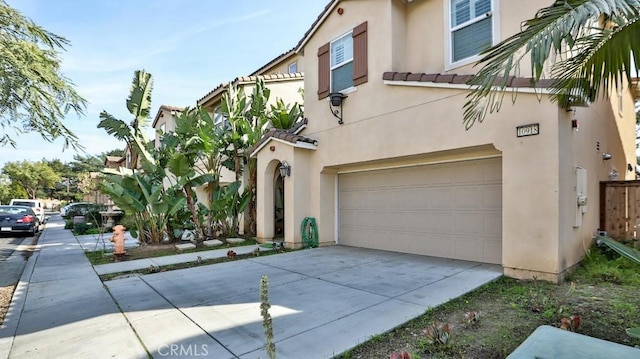 view of front facade with concrete driveway, a tile roof, an attached garage, and stucco siding