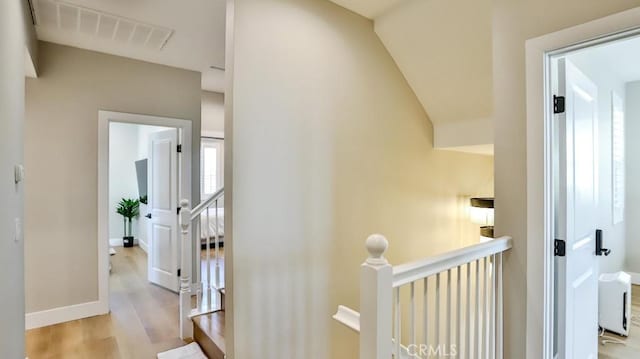 hall featuring light wood-type flooring, baseboards, visible vents, and an upstairs landing