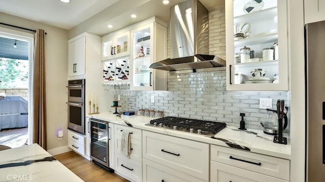 kitchen featuring glass insert cabinets, beverage cooler, white cabinetry, and wall chimney range hood