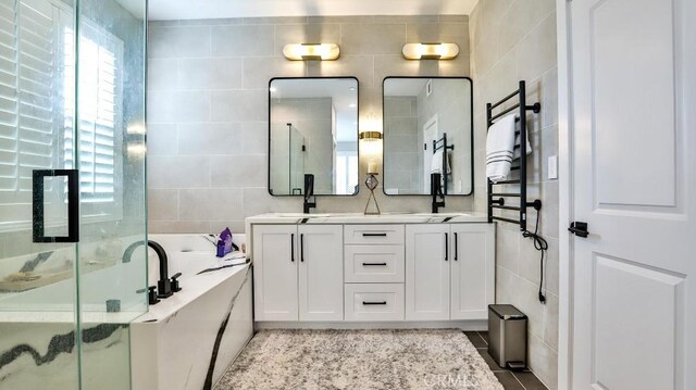 bathroom with double vanity, a bath, a sink, a shower stall, and tile walls