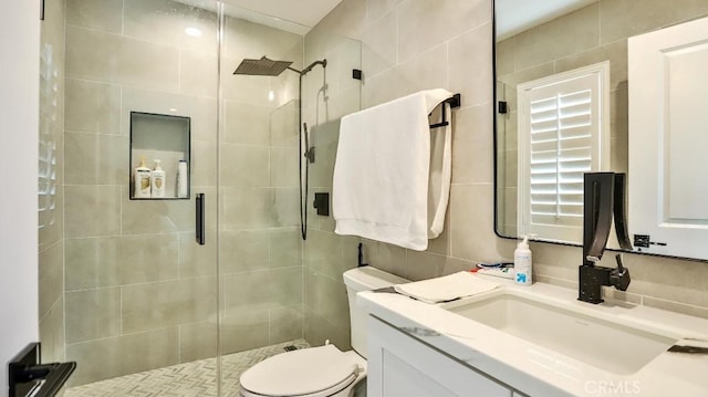 bathroom with a stall shower, tile walls, vanity, and toilet