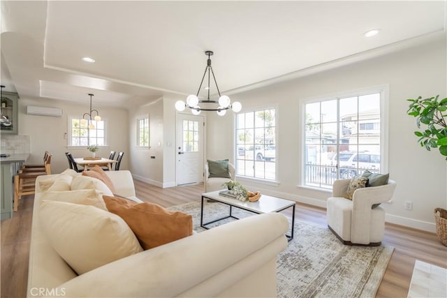 living room featuring a wall unit AC, light wood-style floors, and a notable chandelier