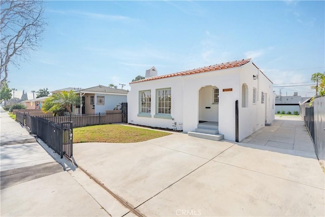 mediterranean / spanish-style house featuring a fenced front yard, a front yard, a tile roof, and stucco siding