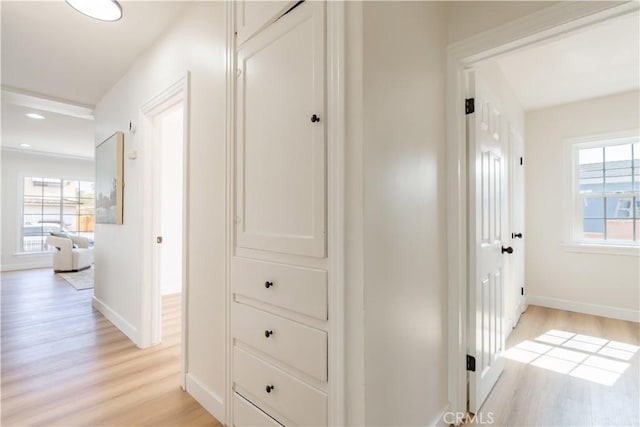 corridor with light wood finished floors, a wealth of natural light, and baseboards