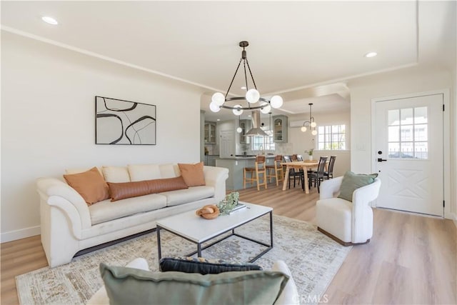 living area featuring recessed lighting, light wood-style flooring, ornamental molding, a chandelier, and baseboards