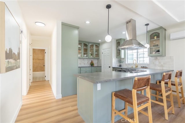 kitchen featuring pendant lighting, island exhaust hood, dark countertops, glass insert cabinets, and a peninsula