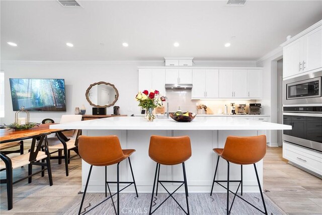 kitchen with stainless steel appliances, a kitchen island with sink, light countertops, and under cabinet range hood