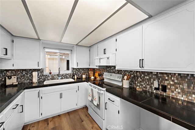 kitchen with white electric range oven, dark countertops, wood finished floors, white cabinetry, and a sink