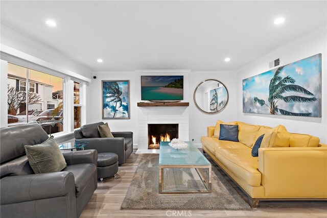 living room featuring recessed lighting, a fireplace, crown molding, and wood finished floors