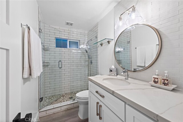 bathroom featuring visible vents, toilet, wood finished floors, vanity, and a shower stall