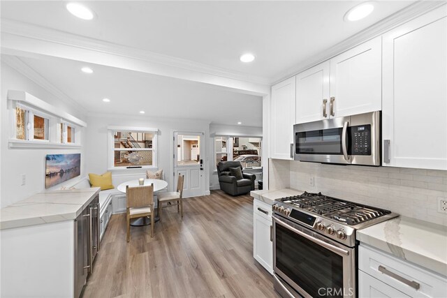 kitchen with white cabinets, appliances with stainless steel finishes, ornamental molding, light stone countertops, and light wood-style floors