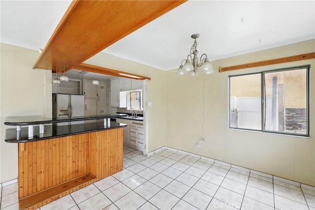 kitchen with a chandelier, dark countertops, a sink, white refrigerator with ice dispenser, and light tile patterned floors