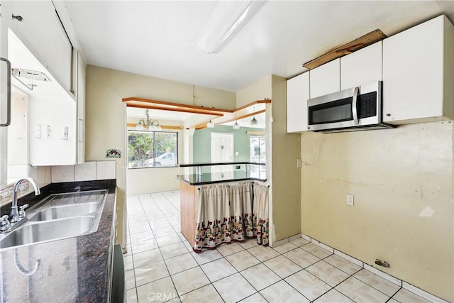 kitchen featuring light tile patterned flooring, stainless steel microwave, dark countertops, white cabinetry, and a sink