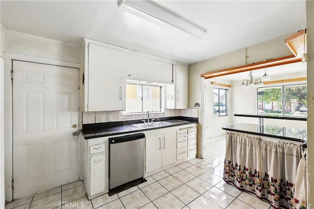 kitchen featuring stainless steel dishwasher, a sink, dark countertops, light tile patterned flooring, and white cabinets