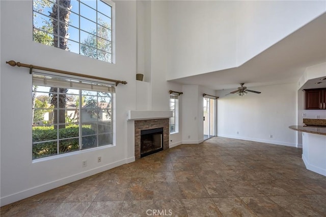 unfurnished living room featuring ceiling fan, a fireplace, a towering ceiling, and baseboards