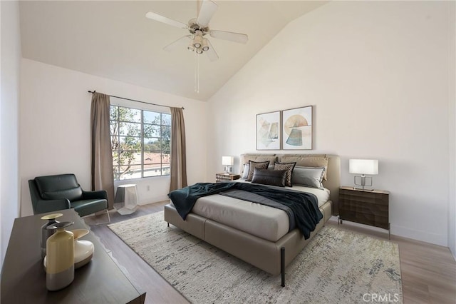 bedroom with light wood-type flooring, baseboards, high vaulted ceiling, and a ceiling fan