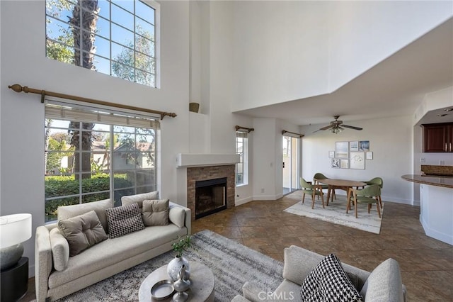 living area featuring a towering ceiling, ceiling fan, a fireplace, and baseboards