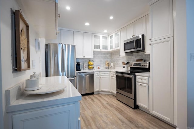 kitchen with stainless steel appliances, light countertops, light wood finished floors, tasteful backsplash, and glass insert cabinets