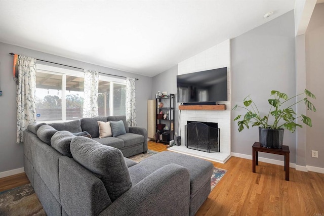 living area featuring a brick fireplace, baseboards, vaulted ceiling, and wood finished floors