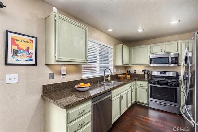 kitchen featuring stainless steel appliances, dark stone countertops, a sink, and green cabinetry