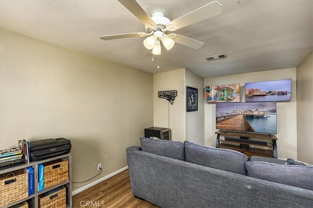 living room with dark wood-style floors, visible vents, ceiling fan, a textured ceiling, and baseboards