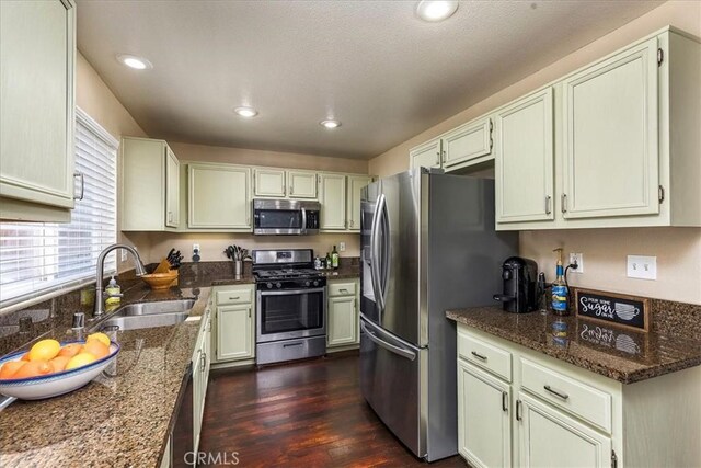 kitchen featuring recessed lighting, stainless steel appliances, a sink, dark stone counters, and dark wood finished floors