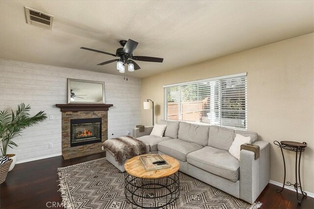 living area featuring dark wood-style flooring, a fireplace, visible vents, ceiling fan, and baseboards