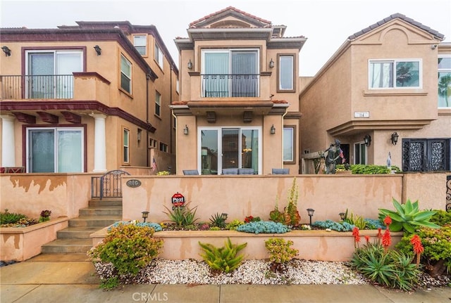 multi unit property featuring a tiled roof, a fenced front yard, a balcony, and stucco siding