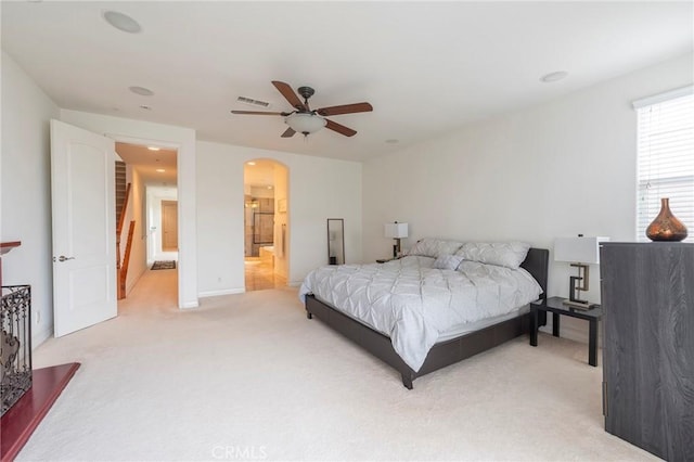 bedroom featuring visible vents, arched walkways, connected bathroom, a ceiling fan, and carpet