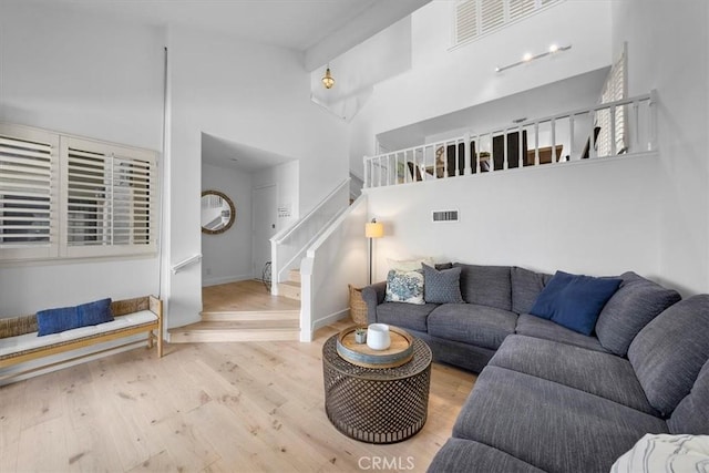 living area with baseboards, visible vents, a towering ceiling, stairway, and wood finished floors