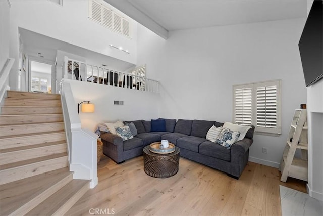 living room with stairs, a high ceiling, light wood-type flooring, and baseboards