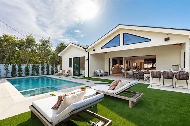 back of house featuring outdoor lounge area, a patio area, a fenced in pool, and stucco siding