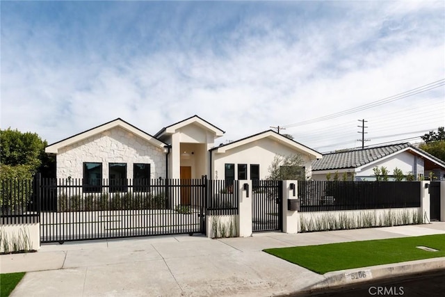 view of front facade featuring a gate, stone siding, a fenced front yard, and stucco siding