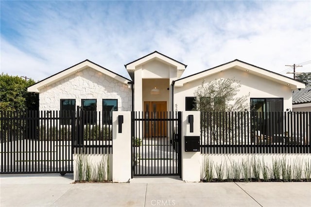 view of front of home featuring stucco siding, stone siding, a fenced front yard, and a gate