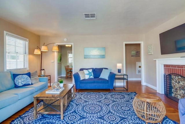 living area with a brick fireplace, visible vents, baseboards, and wood finished floors