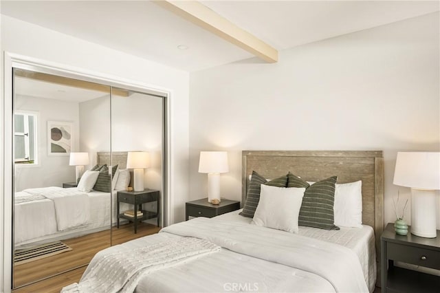 bedroom with a closet, beam ceiling, and wood finished floors