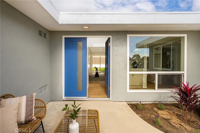 entrance to property featuring visible vents, a patio, and stucco siding