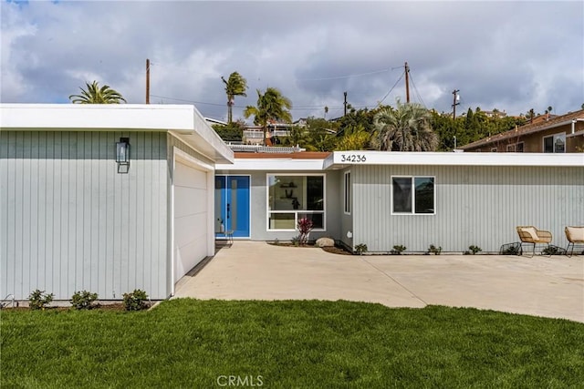 rear view of property featuring a garage, a lawn, and a patio