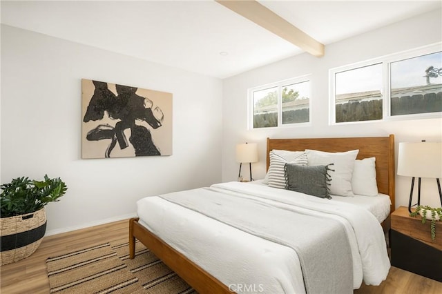 bedroom with wood finished floors, beam ceiling, and baseboards