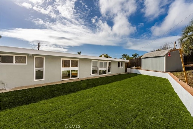 back of house with a yard, stucco siding, fence, a shed, and an outdoor structure