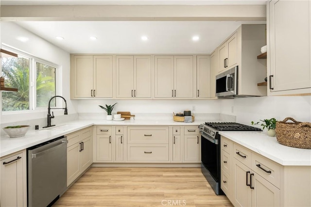 kitchen featuring light wood-style flooring, stainless steel appliances, a sink, light countertops, and open shelves