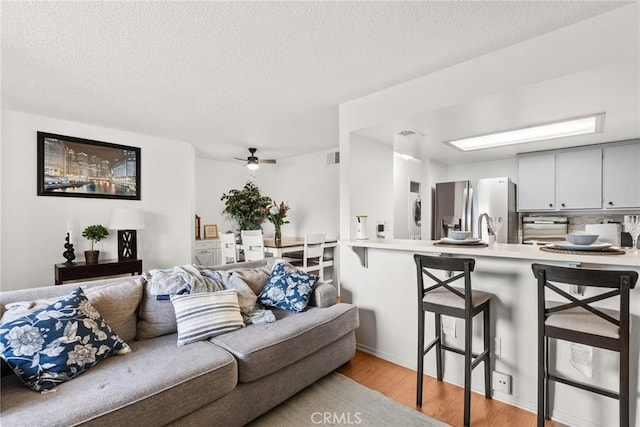 living room with light wood-style flooring, a ceiling fan, and a textured ceiling