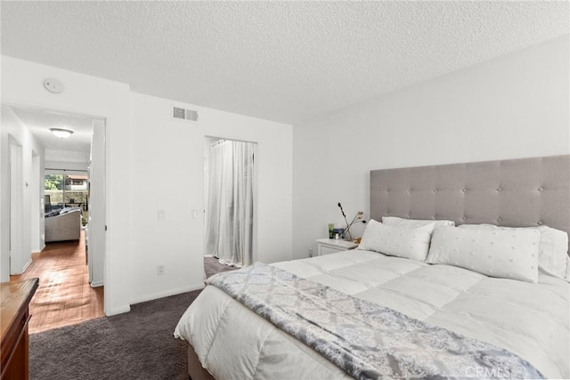 bedroom with visible vents, dark carpet, a textured ceiling, and baseboards